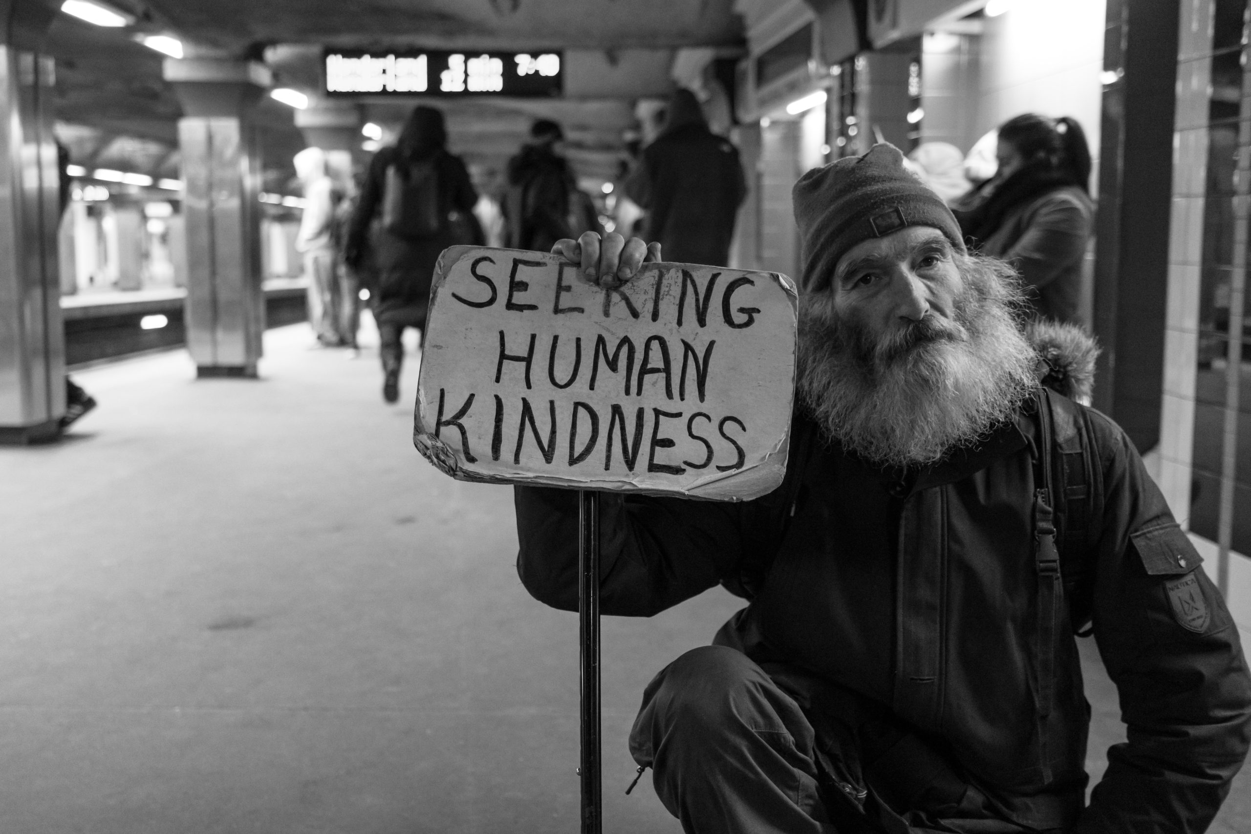 homeless man holding sign that says seeking human kindness